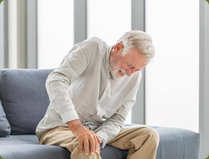 Older man on a sofa holding a stiff knee