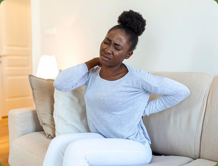 Woman on a sofa holding her neck and lower back in pain
